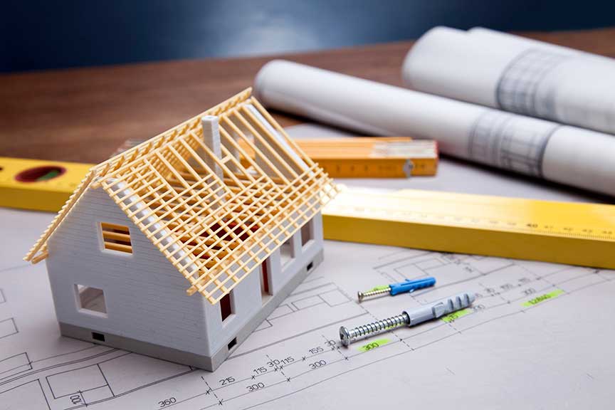 A small model of a new house construction on top of construction plans with a level in the background.